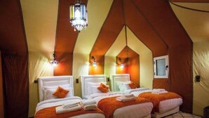 Une pièce chaleureuse avec trois lits, chacun agrémenté de draps blancs et de touches de couleur orange, sous un plafond en pente éclairé par des luminaires décoratifs.