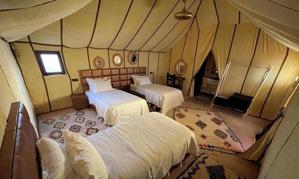 A luxury tented accommodation with two beds, a small window, and a patterned rug.
