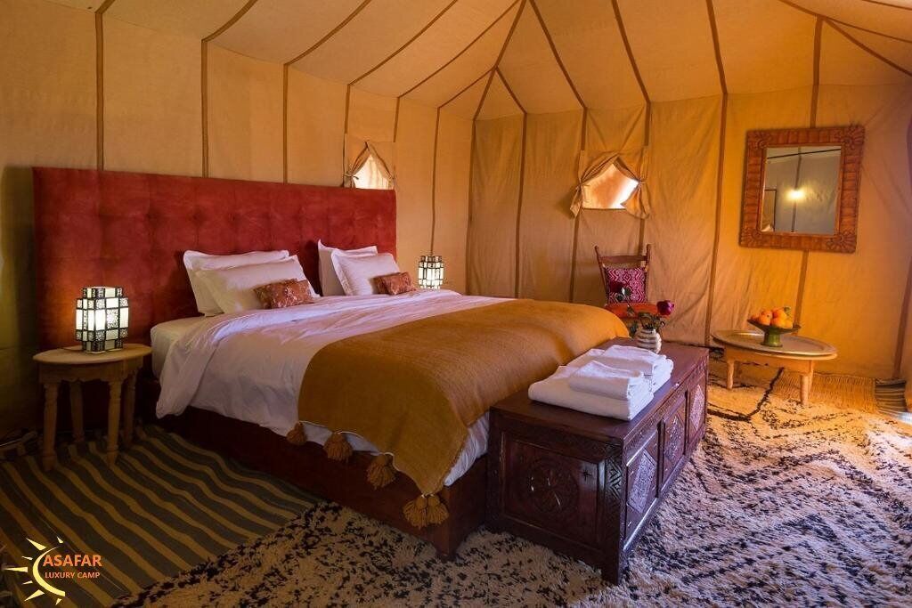 Una lujosa habitación tipo tienda con una cama grande, dos lámparas de noche, una mesita de madera y una pequeña mesa redonda con un jarrón de flores.