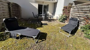 A patio with two lounge chairs, a table, and chairs, a wooden fence, and a balcony with a railing. - 239 - Holiday home for 4 people – Domaine des Sables (SOULAC SUR MER)