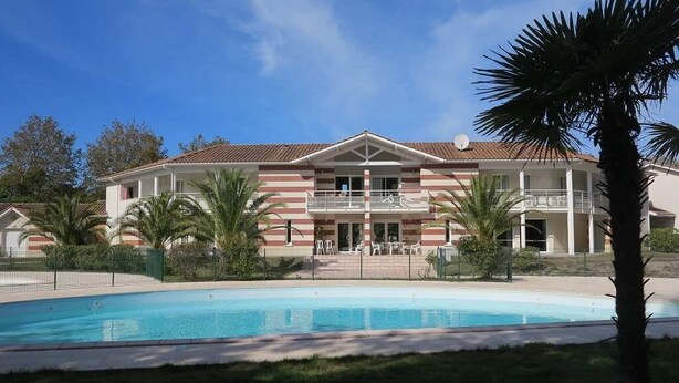 A hotel with a swimming pool, a covered patio, and palm trees. - 239 - Holiday home for 4 people – Domaine des Sables (SOULAC SUR MER)