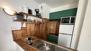 A kitchen with wooden cabinetry, a stainless steel sink, a microwave, and a refrigerator. - 239 - Holiday home for 4 people – Domaine des Sables (SOULAC SUR MER)