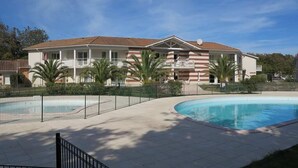 A hotel with a swimming pool, a fenced patio area, and palm trees. - 239 - Holiday home for 4 people – Domaine des Sables (SOULAC SUR MER)