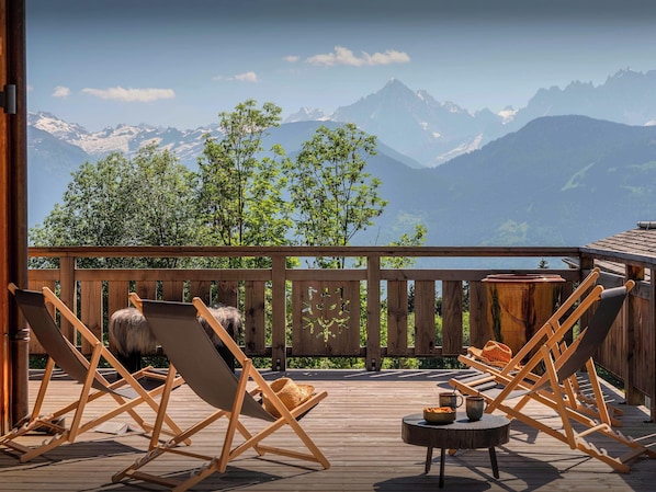 Una terraza de madera con sillones de descanso y una pequeña mesa, con vistas a una cordillera.