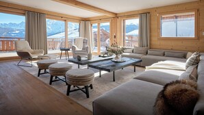 Un salon spacieux doté d’un plancher en bois, d’un canapé, d’un fauteuil, d’une table basse et offrant une vue sur les montagnes grâce à de grandes fenêtres.