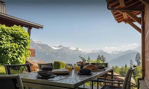 Mesa al aire libre con vista a la montaña, un pérgola de madera y un arbusto verde exuberante.