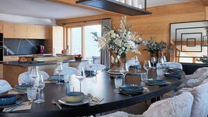 Une cuisine moderne avec des meubles en bois, un îlot central doté de sièges et un coin repas avec une table sombre, dressée pour six personnes.