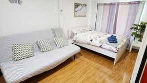 Ett rum med en randig soffa, en säng med ett blommigt överkast, ett litet bord och en krukväxt.