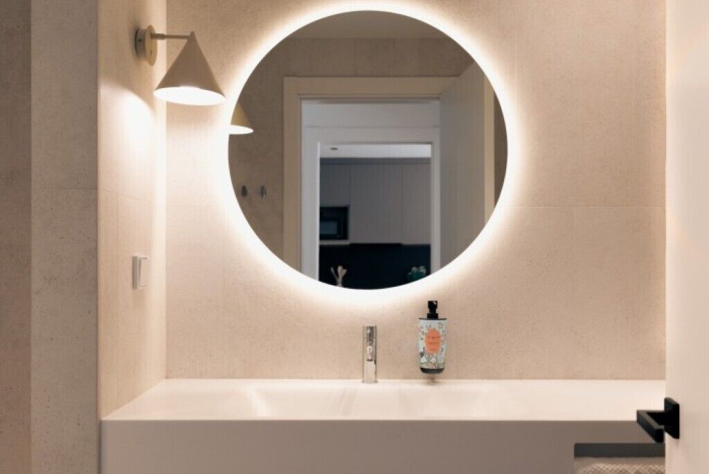 A bathroom with a round mirror, a sink, and a hand soap dispenser.