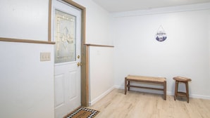 Un couloir épuré et minimaliste, avec un banc en bois et un petit tabouret, un paillasson et une enseigne fixée au mur.