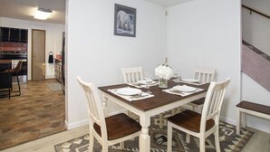 A dining area with a wooden table, white chairs, and a rug. - Cozy Bear Den Rustic Cabin Central Located (Fairbanks)