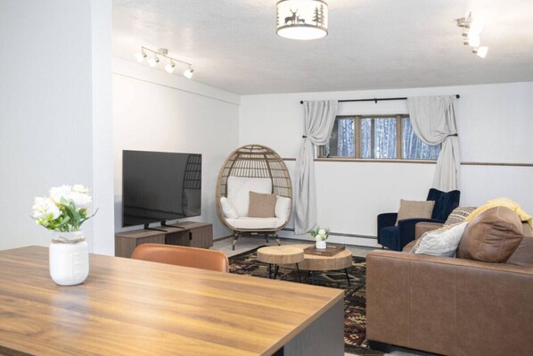 A living room with a TV, a round wicker chair, a sofa, and a dining table.