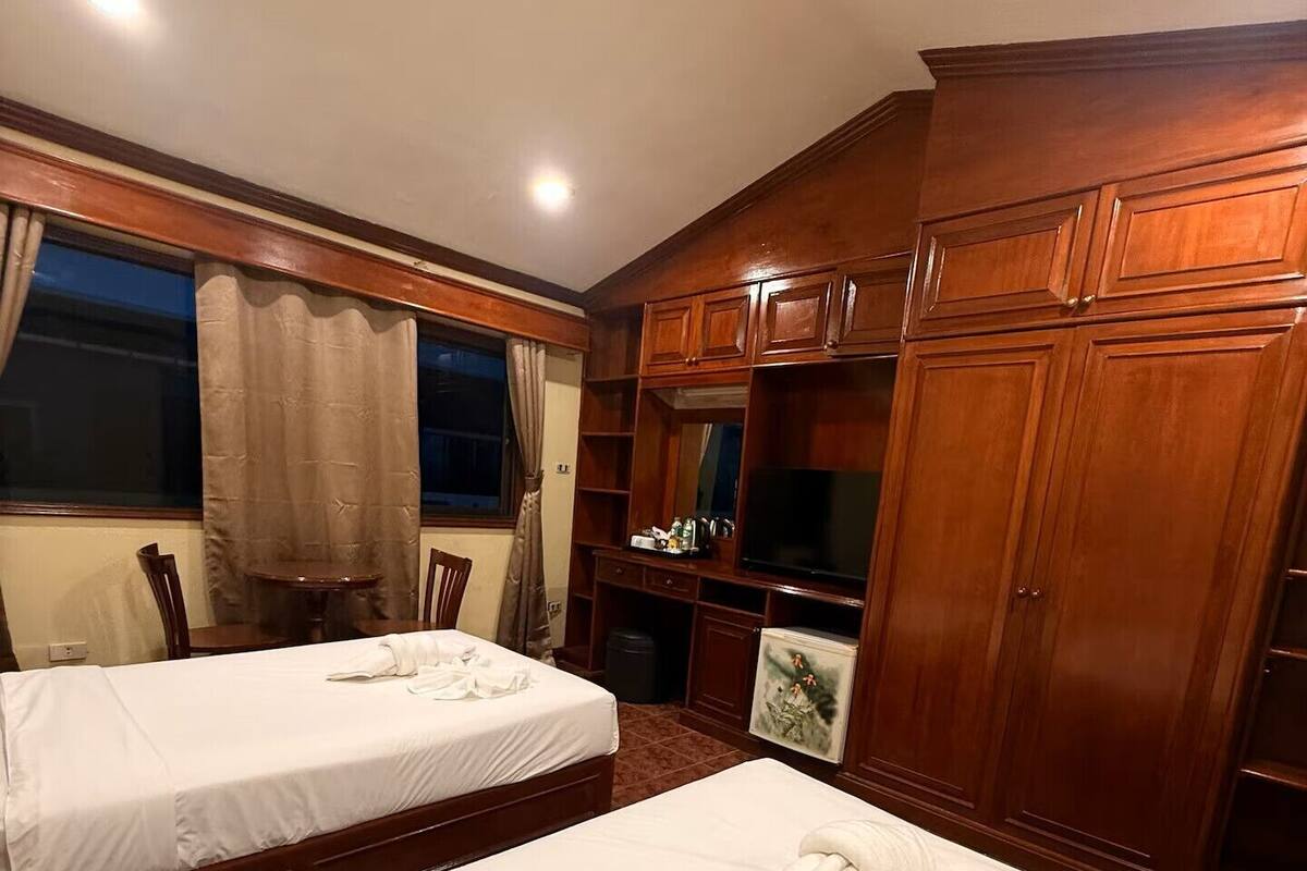 Ein Hotelzimmer mit zwei Betten, Holzschränken, einem Fernseher und einem Gemälde an der Wand.