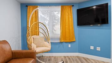 A room with a blue wall, a television mounted on the wall, a hanging chair, and a brown leather sofa.