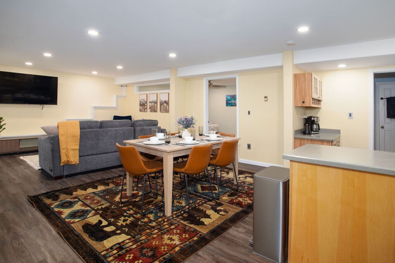 Una sala de estar moderna con un sofá, una mesa de comedor con sillas, una zona de cocina y un televisor montado en la pared.