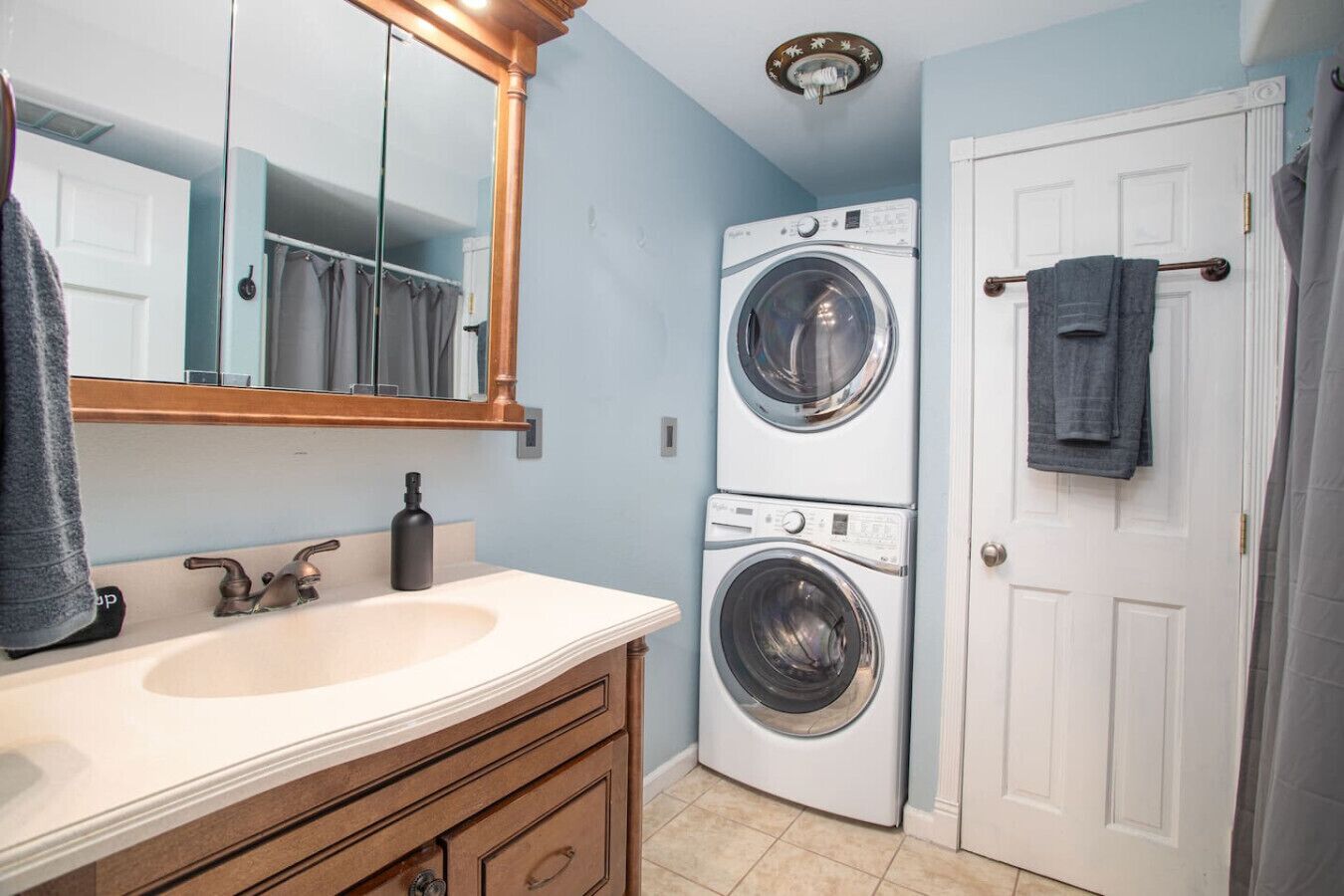 A compact bathroom with a sink, mirror, and stacked washing machines.