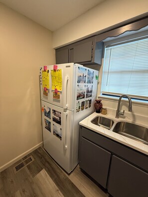 A kitchen with a refrigerator, a sink, and a window with blinds.