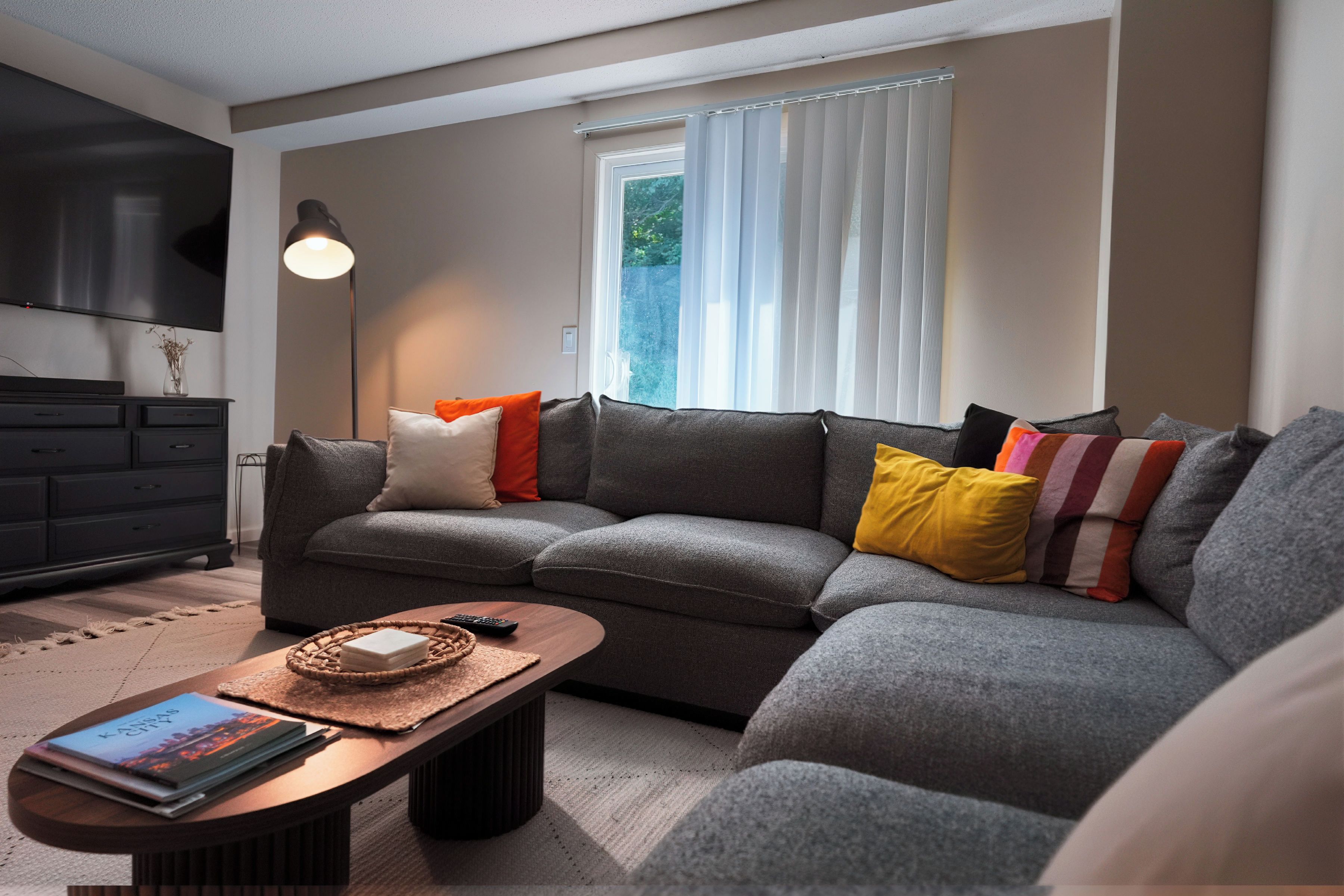 Una sala de estar moderna con un sofá seccional gris, una mesa de centro de madera y una lámpara de pie.