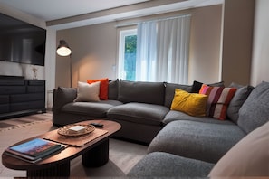 A modern living room with a grey sectional sofa, a wooden coffee table, and a floor lamp. - Relax & Recharge • Cozy Retreat in Rosedale, KS (Kansas City)