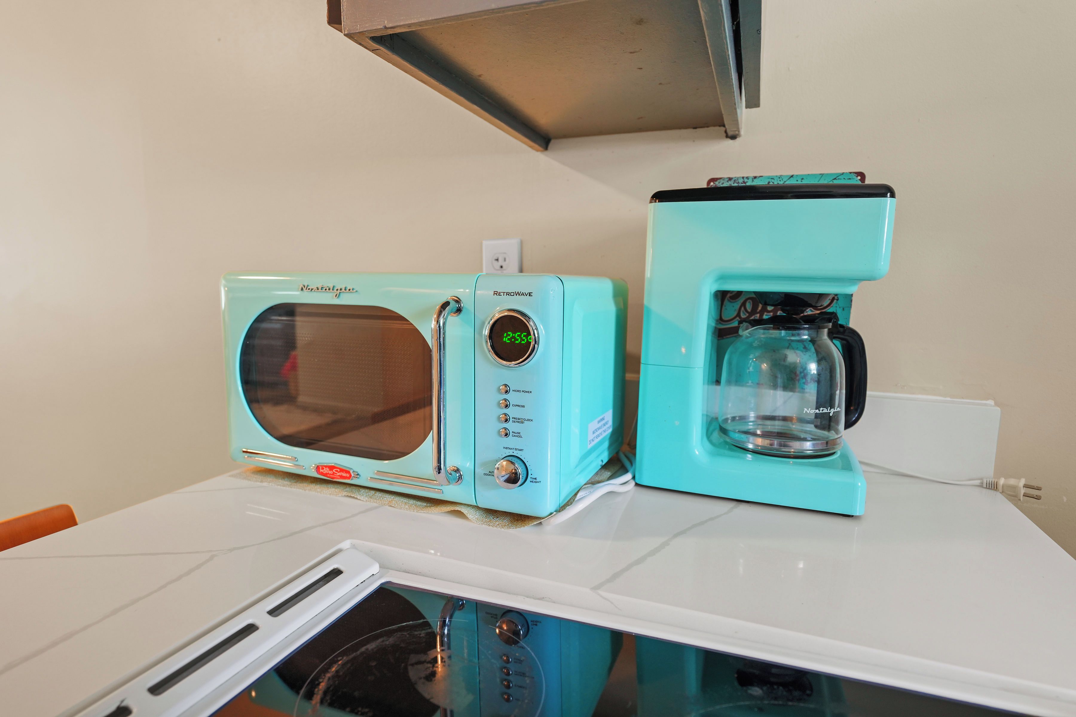 A retro-style kitchen with a turquoise microwave and coffee maker on a white countertop.