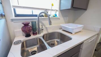 A kitchen with a double stainless steel sink, a window above the sink, and a white basin on the countertop.