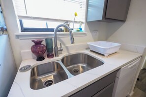 A kitchen with a double stainless steel sink, a window above the sink, and a white basin on the countertop.