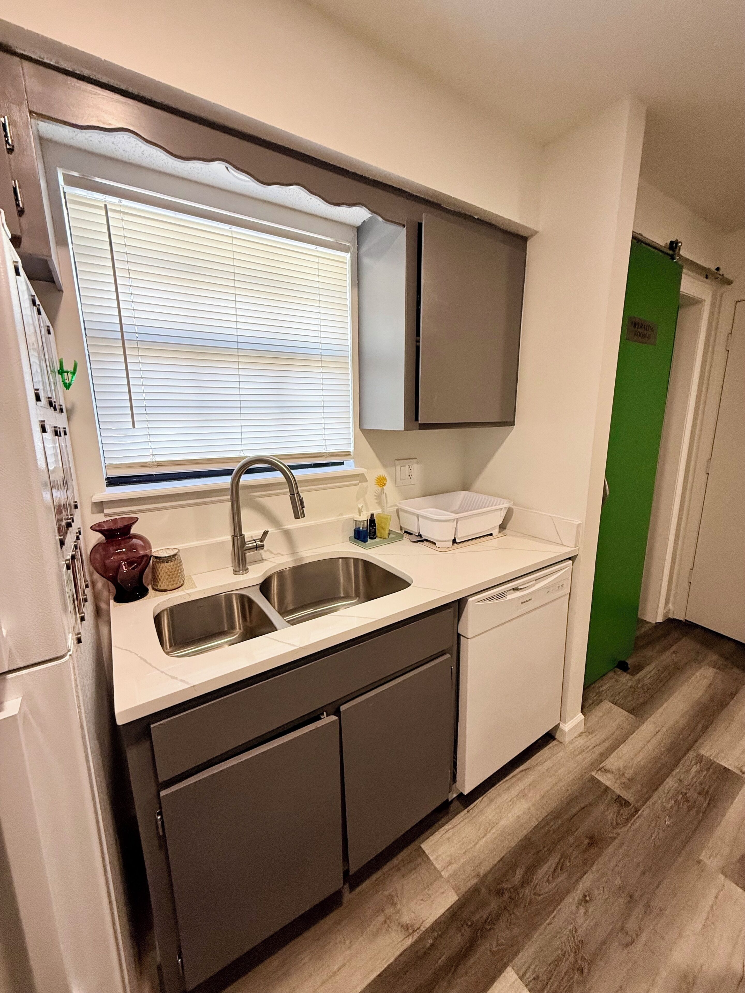 A compact kitchen with a sink, dishwasher, and a window with blinds.