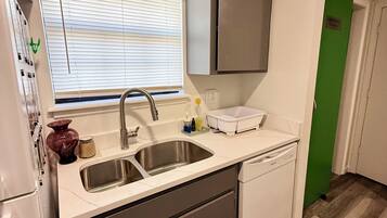 A compact kitchen with a sink, dishwasher, and a window with blinds.