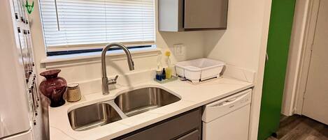 A compact kitchen with a sink, dishwasher, and a window with blinds.