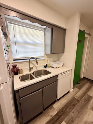A compact kitchen with a sink, dishwasher, and a window with blinds.
