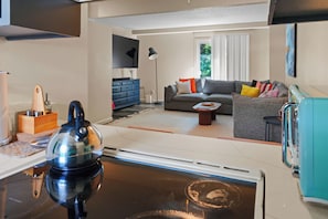 A modern kitchen with a kettle, a dining table with a basket, and a sofa in the living area.