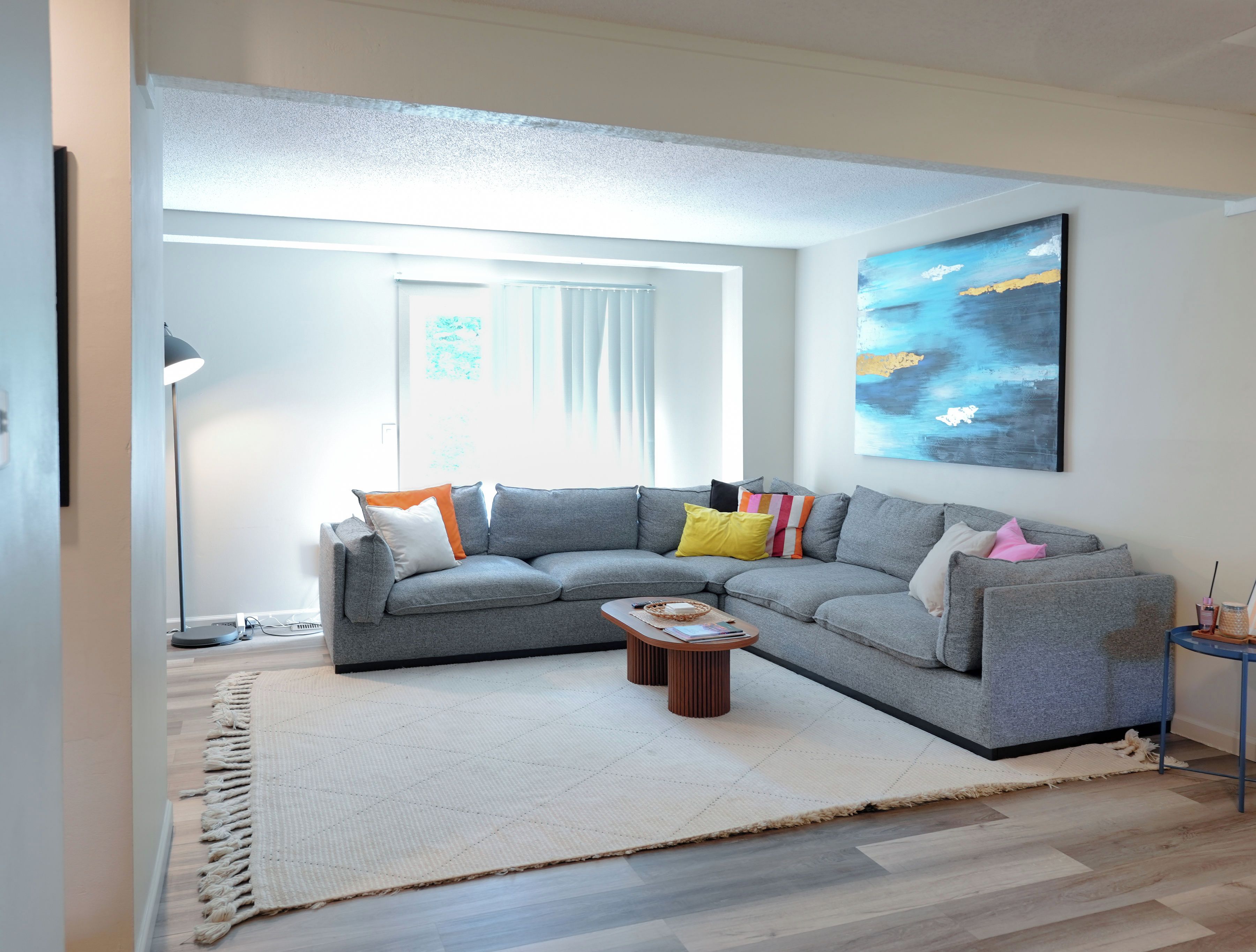 A modern living room with a grey sectional sofa, a coffee table, and a large abstract painting on the wall.