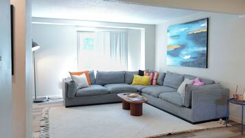 A modern living room with a grey sectional sofa, a coffee table, and a large abstract painting on the wall.