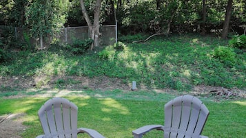 Two Adirondack chairs on a red mat with a small table, surrounded by a grassy area and trees.