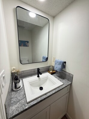 A bathroom with a white sink, black faucet, and a mirror above it. There is a towel rack with a blue towel and a small decorative item on the countertop.