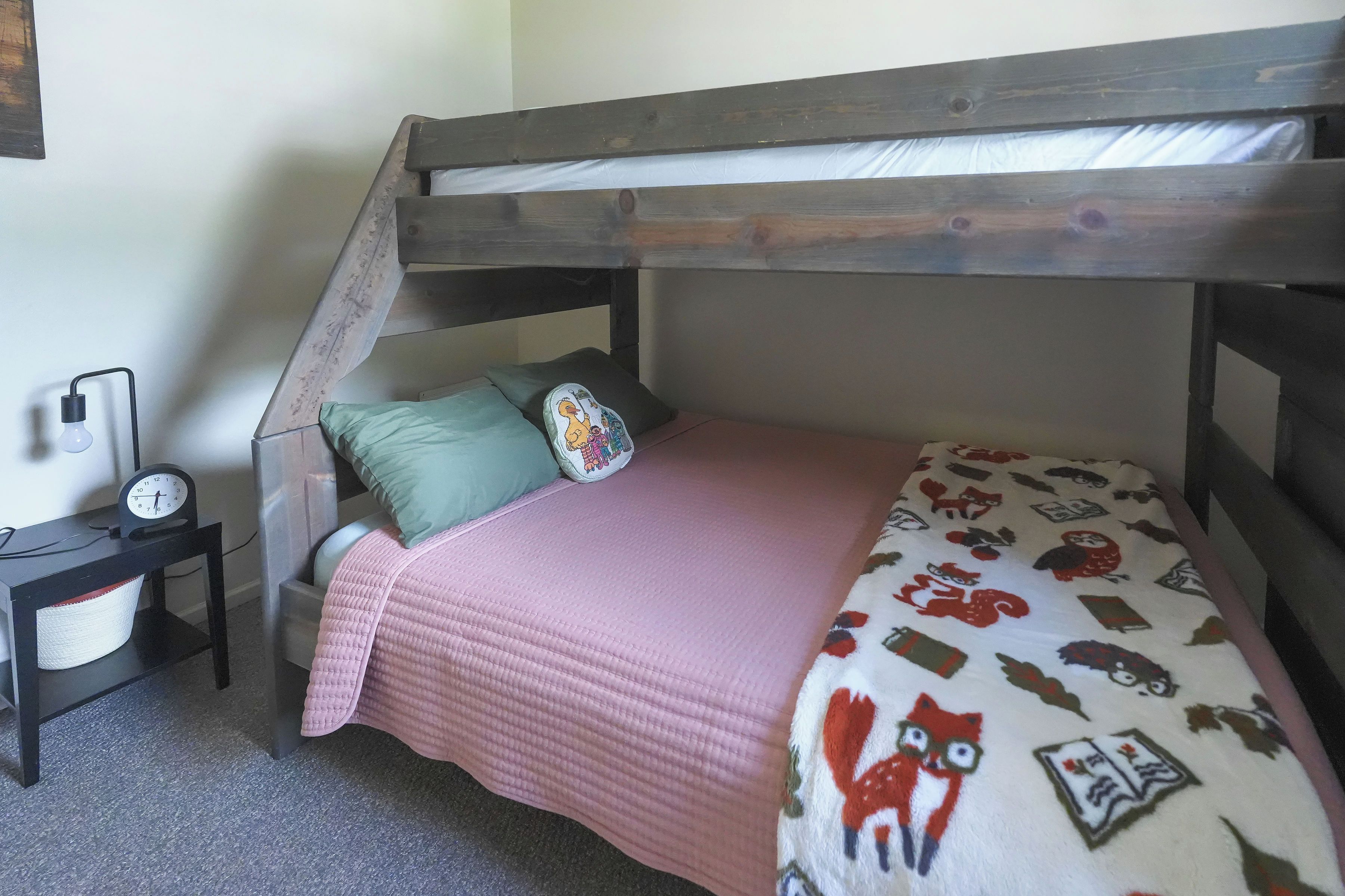 Una cama litera con cabecera de madera, una mesita de noche con lámpara y un reloj de pared.