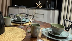 A dining table set with plates, glasses, and a kettle, with a kitchen in the background. - Seaside Studio on the ecological route of Milagres (Porto de Pedras)