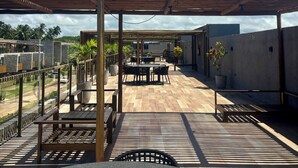 An outdoor patio with a wooden pergola, tables, chairs, and potted plants. - Seaside Studio on the ecological route of Milagres (Porto de Pedras)