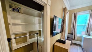 A room with a sliding door, a television mounted on the wall, a small wooden cabinet, and a window with curtains. - Nice large room in Federal Hill (Providence)