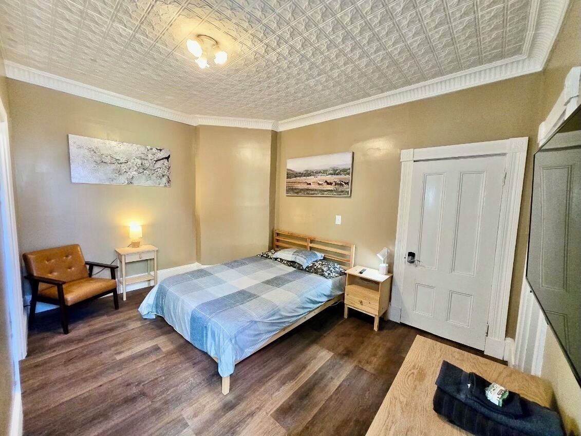 Une chambre à coucher comprenant un lit, une chaise, une table de chevet et une commode, ainsi qu’une porte.