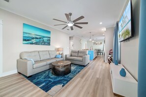 A modern living room with a ceiling fan, a large painting, and a dining area in the background. - Coastal Charm Cottage in the Heart of Foley~Sports Complex~OWA~Beach! (Foley)