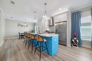 Une cuisine moderne dotée d’un îlot central, de tabourets de bar, d’appareils électroménagers en acier inoxydable et de luminaires suspendus.