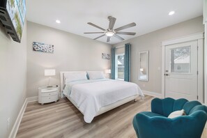 Une chambre à coucher comprenant un lit, une table de chevet, une lampe, un ventilateur de plafond et un fauteuil de couleur turquoise.