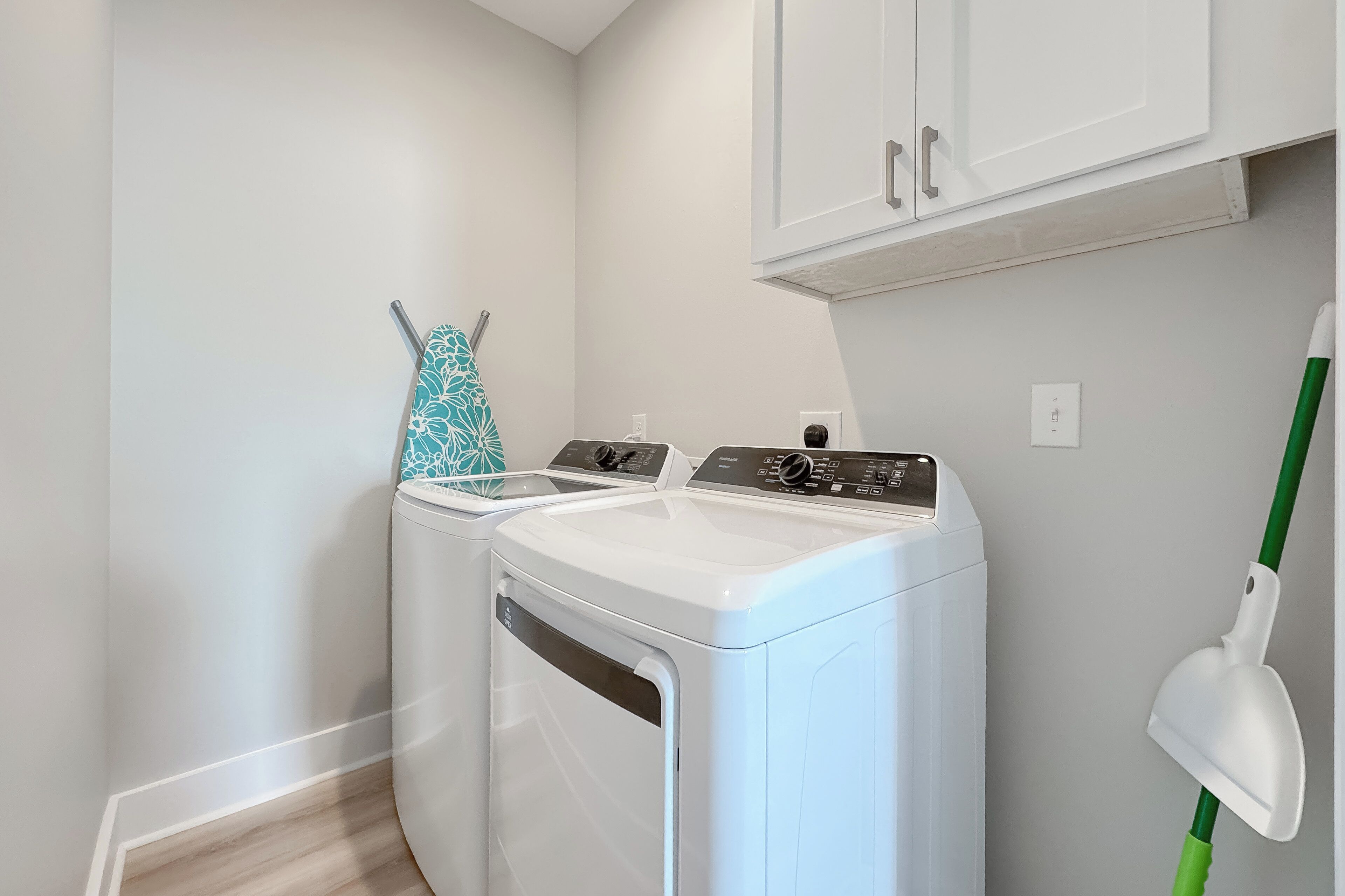 A laundry area with two washing machines, a mop, and white cabinets.