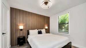 Quarto com cama, abajures, janela com persianas, painel de parede de madeira e luminária de teto.