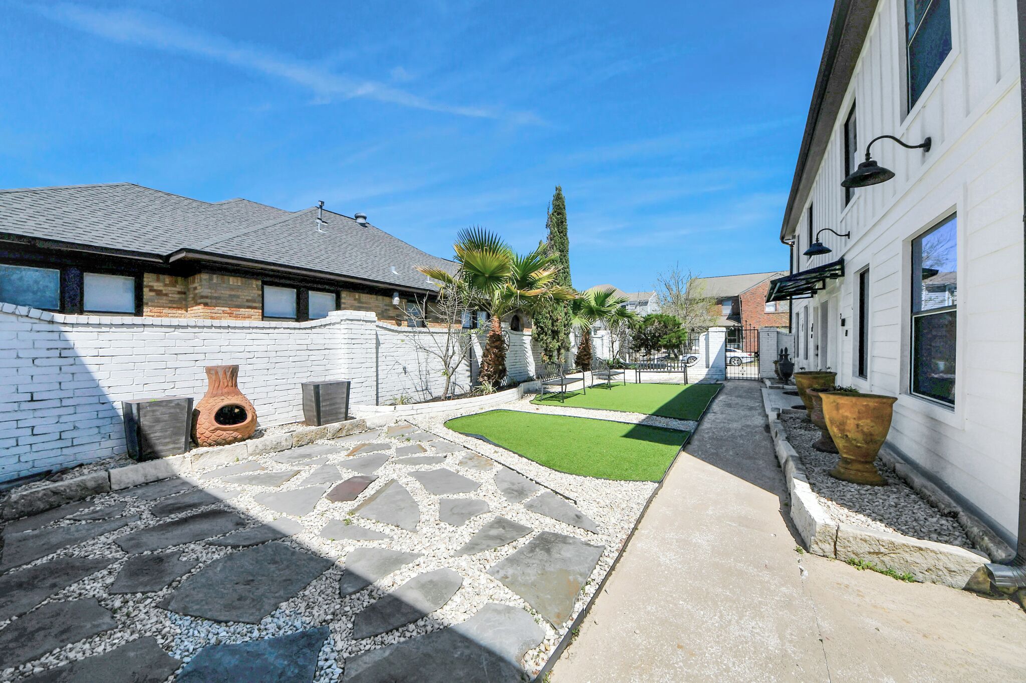 A courtyard with stone pathways, a lawn, and a white building with large windows.