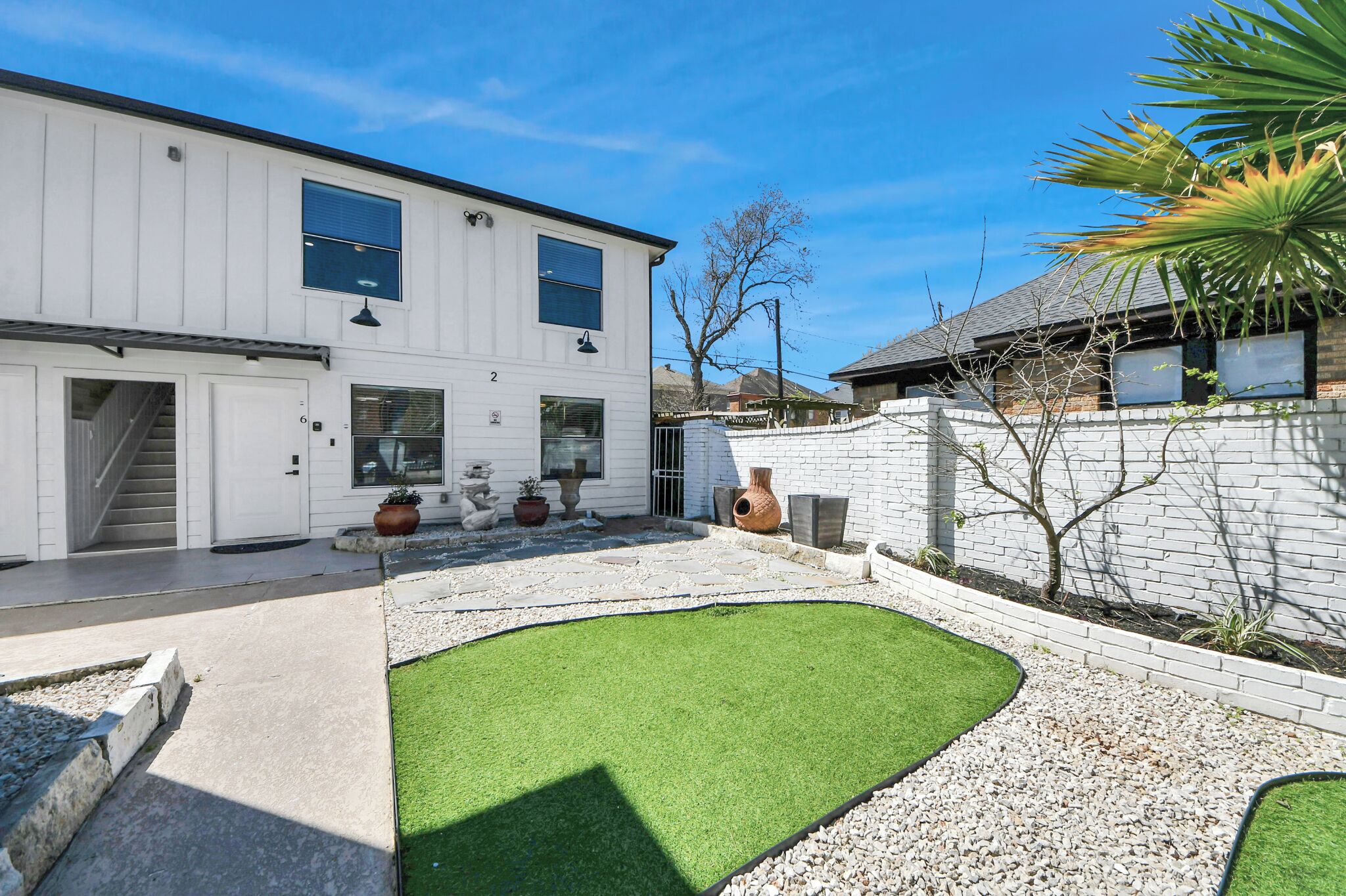 Ein modernes, zweistöckiges Haus mit Terrasse, Rasenfläche und Ziergefäßen.