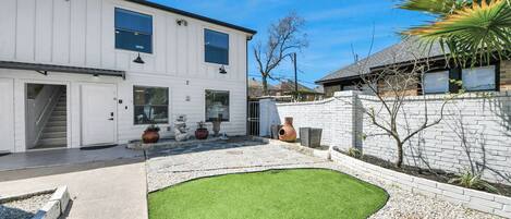 Ein modernes, zweistöckiges Haus mit Terrasse, Rasenfläche und Ziergefäßen.