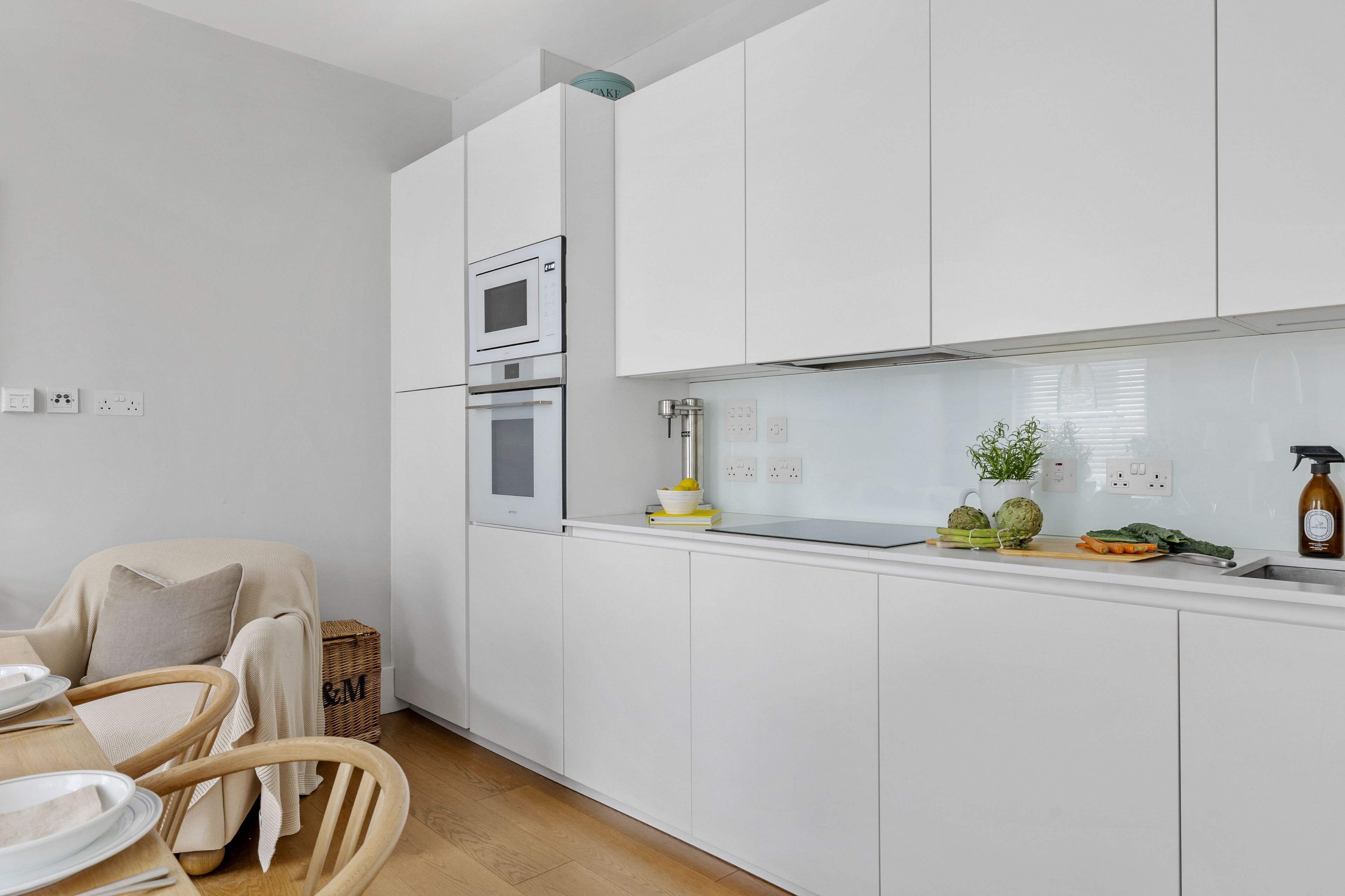 A modern kitchen with white cabinets, a built-in oven, and a countertop with fresh produce.
