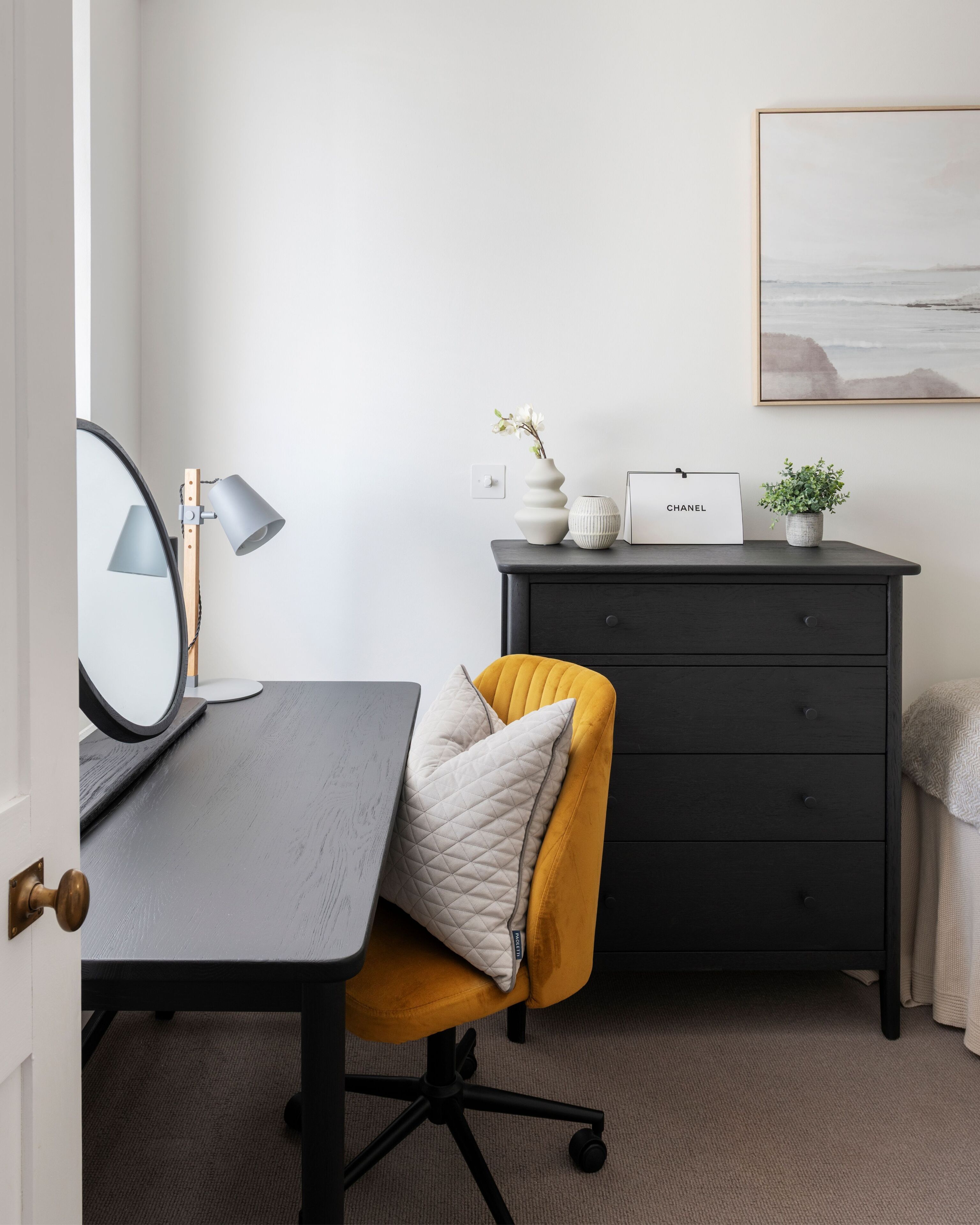 Ein Zimmer mit Schreibtisch, Stuhl, Kommode und einem gerahmten Bild an der Wand.